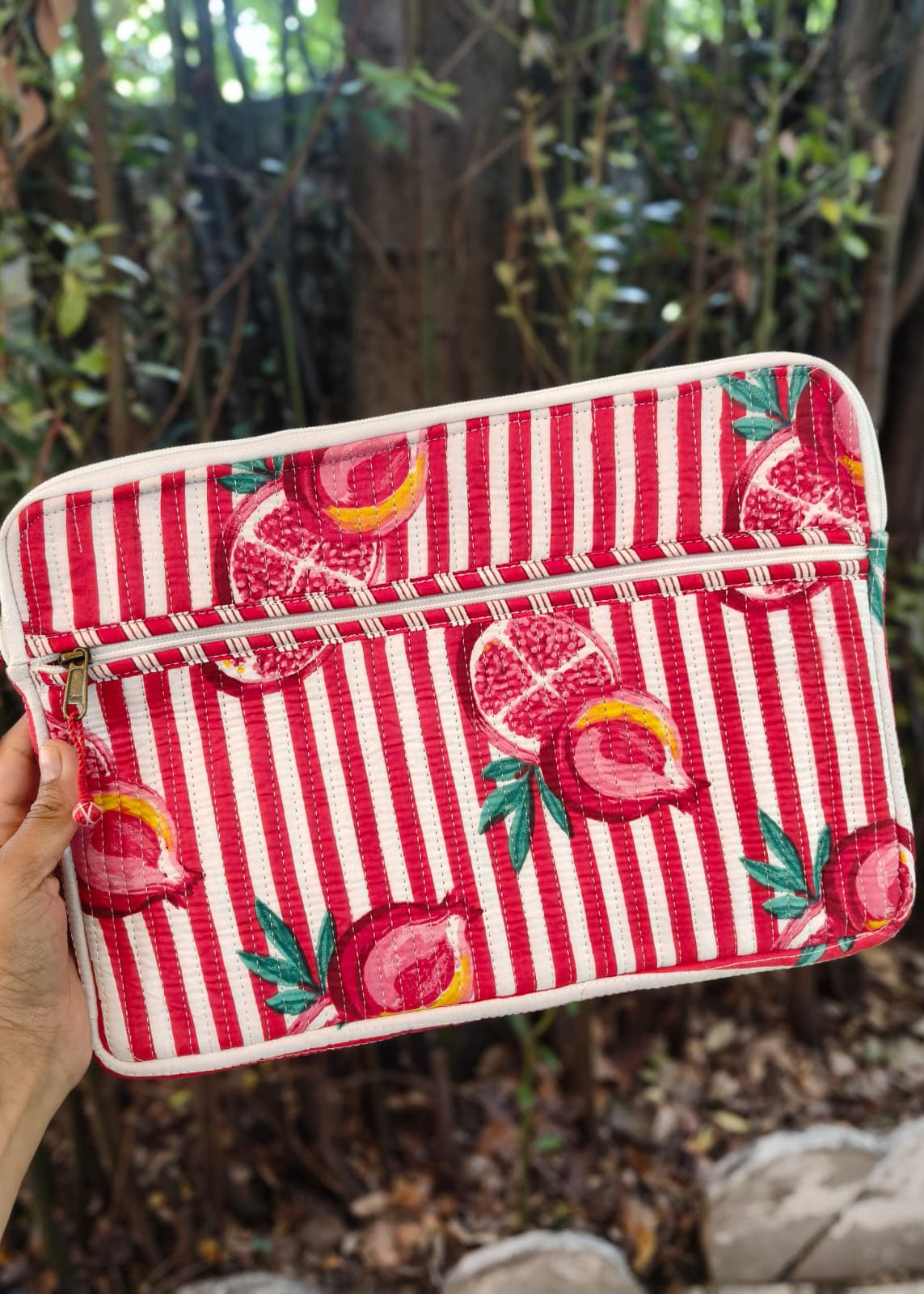Red and white striped pouch with pomegranate design held in front of a natural background
